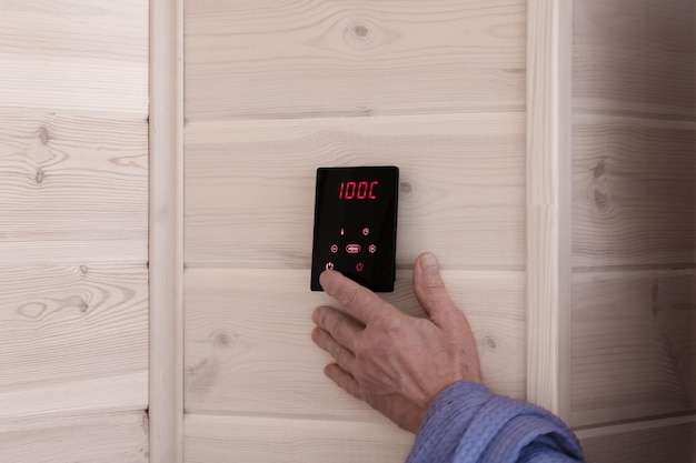 Mannenhand past de temperatuur in de sauna aan op het touchscreen van de afstandsbediening