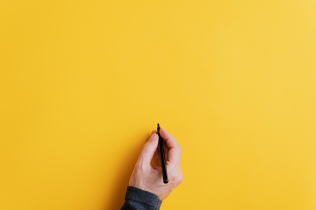 Mannenhand schrijven op een leeg geel oppervlak met zwarte stift