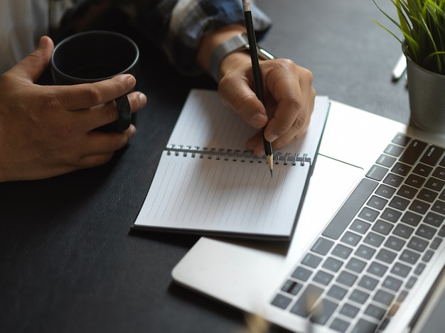 mannenhand schrijven op laptop tijdens het werken met laptop en koffiekopje op werktafel te houden