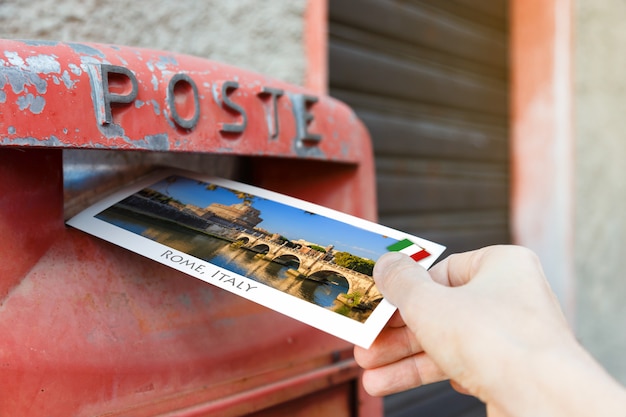 Mannenhand zet een briefkaart in een rode brievenbus in rome, italië, europa