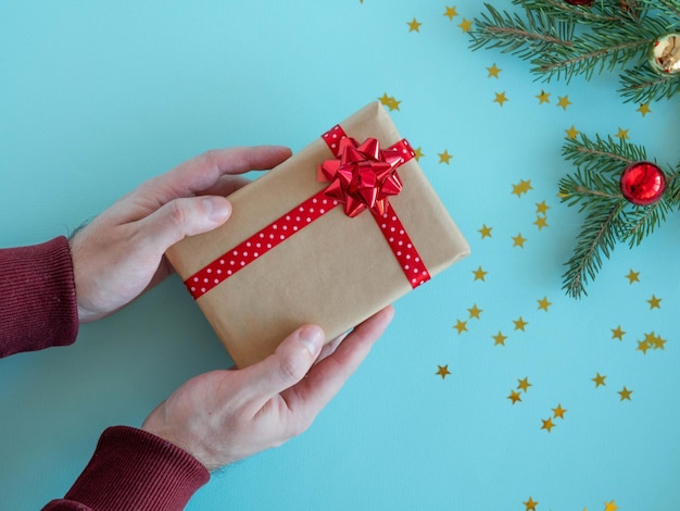 Mannenhanden houden een geschenk vast met een rode strik en een satijnen lint in hun hand op een kerstachtergrond