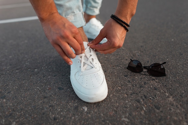 Mannenhanden maken veters recht op witte modieuze leren sneakers. nieuwe collectie stijlvolle herenschoenen en accessoires. detailopname.