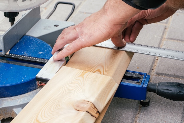 Mannenhanden meten de plank voor het bekleden van het huis met een stalen proefvierkant op een verstekzaag. Bouw- en renovatieconcept