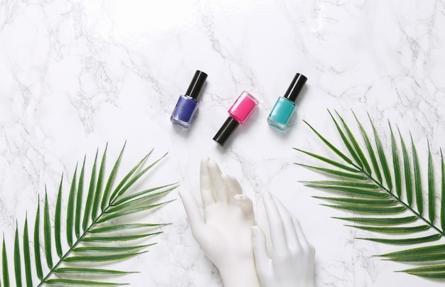 Mannequin hand bottles of nail polish on marble background with palm leaves Beauty layout