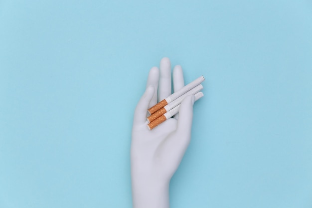 Mannequin hand holding cigarettes on blue background