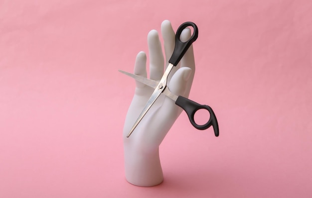 Mannequin hand holding hair scissors on pink background. Minimalism beauty concept