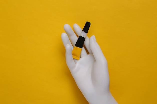 Mannequin's hand holds a tube of glue on a yellow background Top view