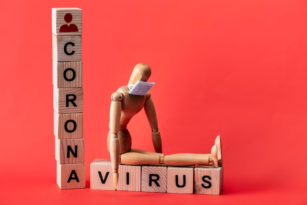 Mannequin in small medical mask near wooden cubes with coronavirus lettering on red