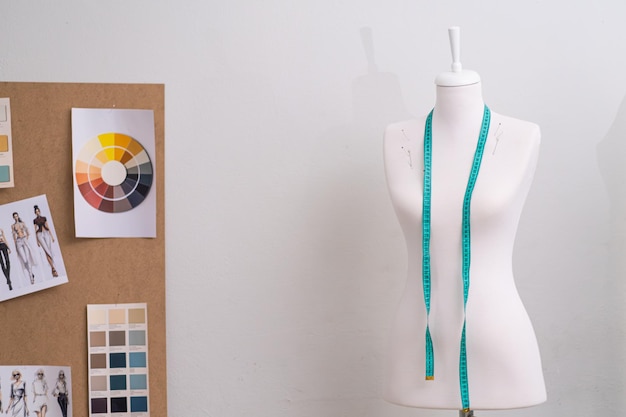 Photo mannequin with tape measure and board with sketches by white wall in sewing studio fashion designer