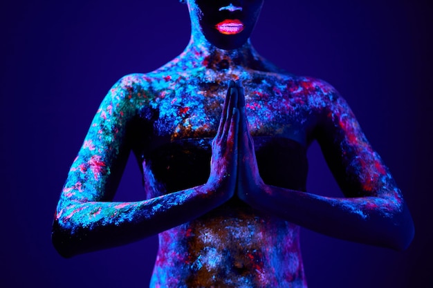 Foto mannequinvrouw in neonlichtmodel met fluorescerende make-up in gebedspositie