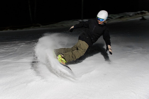 Mannetje dat snowboarder onderaan de berghelling berijdt bij nacht