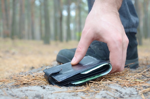 Mannetje die omhoog verloren portefeuille van een grond in de houten weg van de de herfstspar met de hand plukken. het concept van het vinden van een waardevol ding en veel geluk