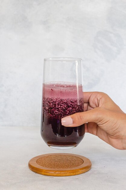 Mano de chica sujetando vaso de cristal con granada de remolacha morada fresco fondo blanco, composiciÃ³n amplia. Bebida Detox dietÃ©tica