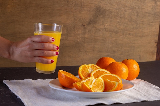 Mano de mujer sostiene un vaso de jugo en una mesa, fondo de fruta de naranja saludable muchas frutas frescas de naranja, vida sana.