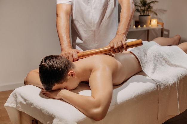 Mans back during traditional thai massage with stick oriental alternative medicine with wooden tools