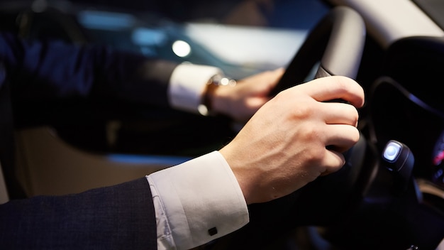 Mans grandi mani su un volante mentre guida un'auto