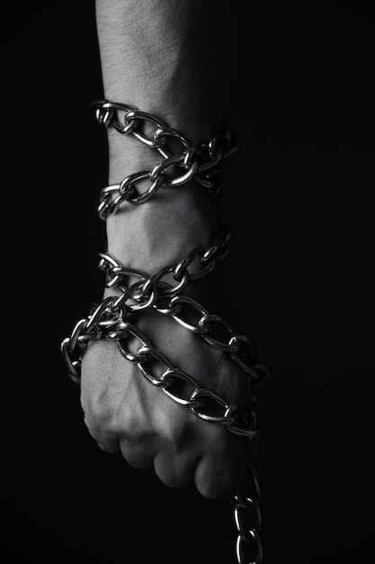 Mans hand entangled with a metal chain concept slavery hostage and freedomBlack and white photo