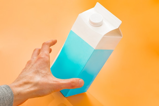 Mans hand grabbing a blue and white paper bag of milk on a orange background Large capacity Grab