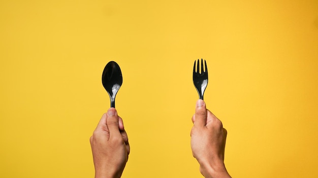 Photo mans hand holding a black spoon and fork on a yellow background