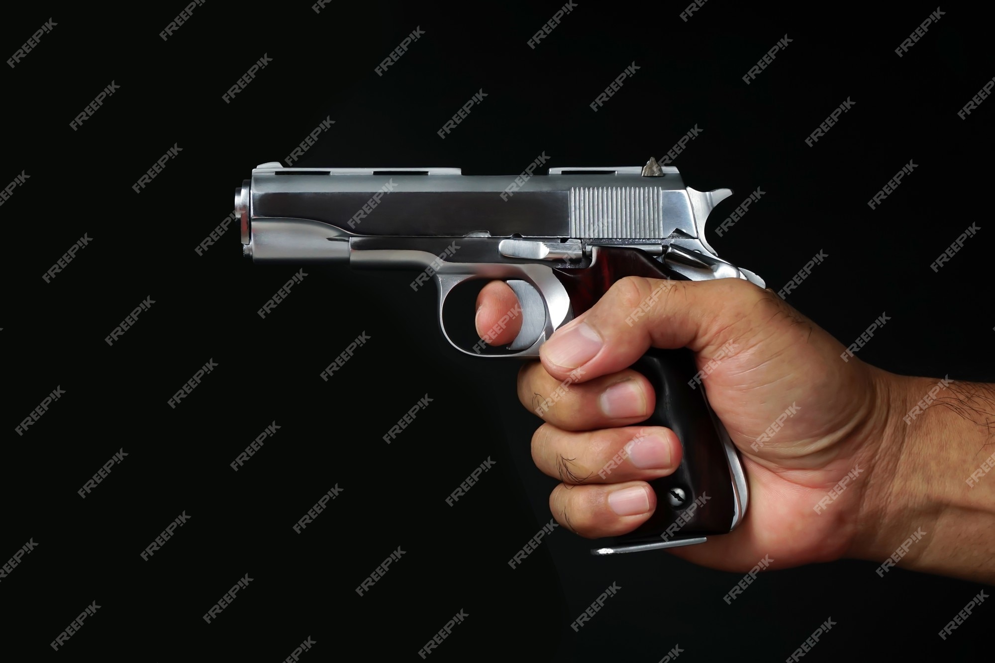 Premium Photo | Mans hand holding a gun on a black background