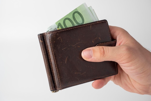 A mans hand holds a brown leather wallet with 100 euro bills sticking out of it on a white background The concept of money wealth wealth