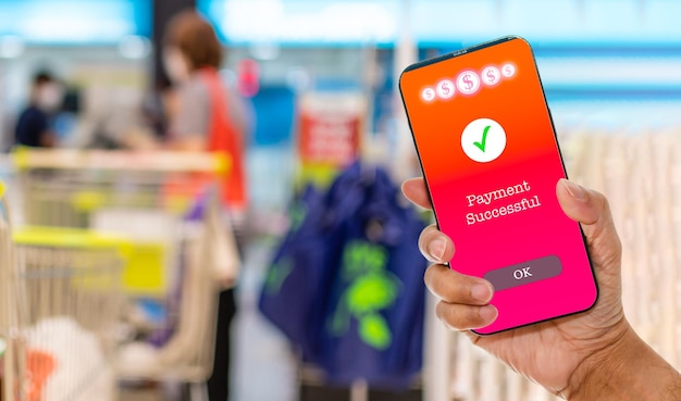 A mans hand holds a smartphone on screen with message Payment Successful in a supermarket Concept of financial transactions with mobile devices Closeup money transfer online blurred background