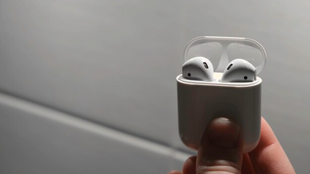 Рука человека помещает наушники AirPods в коробку концепция человек помещает наушники AirPods для зарядки в коробке