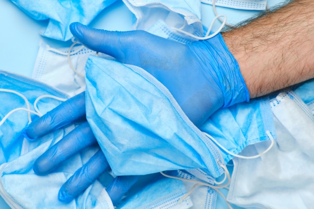 Mans hand in rubber blue glove holding used disposable surgical mask. Medical trash after coronavirus pandemic. End of quarantine.