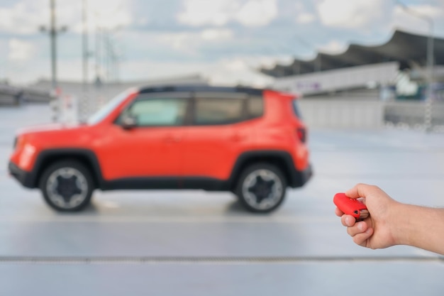 A mans hand uses the key of the remote control of a car parked in the parking lot