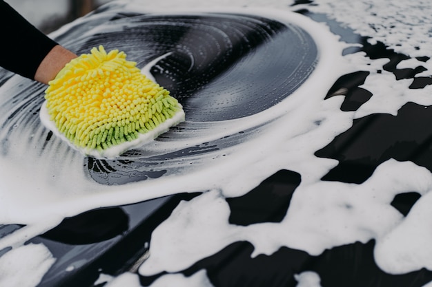 Mans hand wassen zwarte auto met doek en zeepbellen