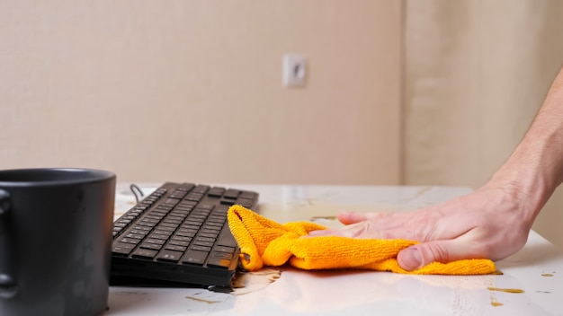 Mans hand wipes spilled coffee from table and keyboard