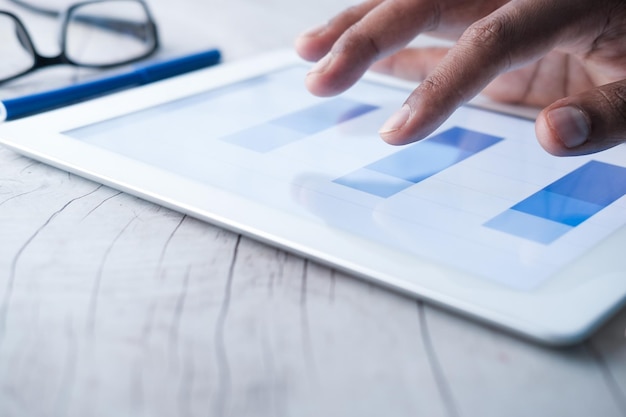 Mans hand working on digital tablet at office desk using self created chart