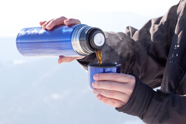 Mans hands pouring fresh hot tea from thermos to cup