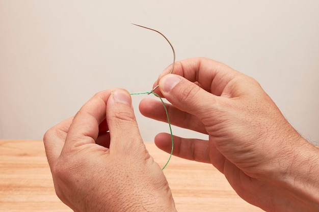 Mans hands threading mattress needle with thick thread