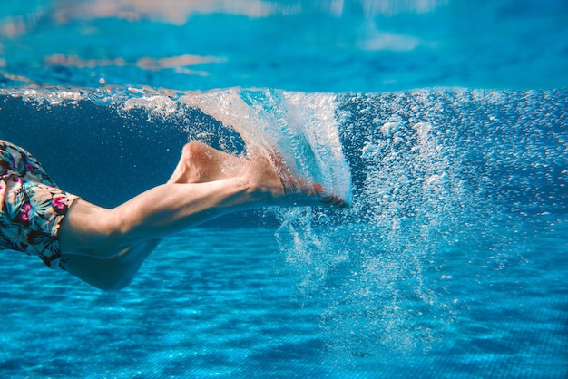 Mans legs swimming underwater in the swimming pool in summer