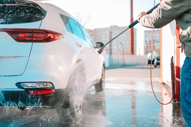 Manual car wash with pressurized water in car wash outside.\
summer car washing. cleaning car using high pressure water. washing\
with soap. close up concept