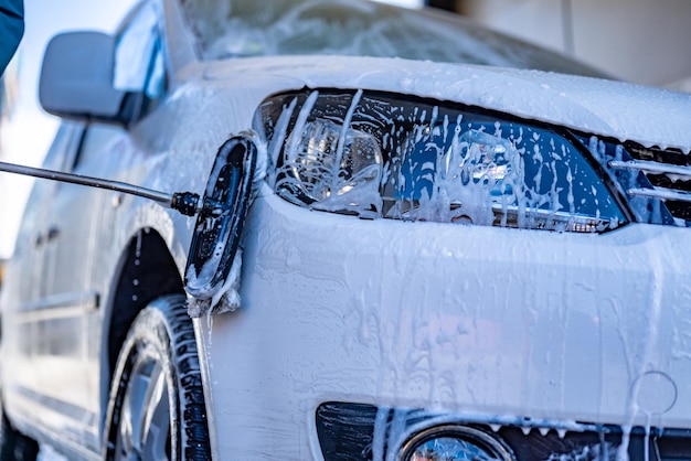 Manual car wash with white soap foam on the body Washing Car Using High Pressure Water