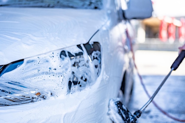 Manual car wash with white soap foam on the body washing car using high pressure water