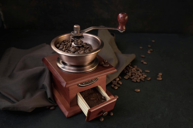 A manual coffee grinder and roasted coffee beans on a black background The vintage coffee grinder