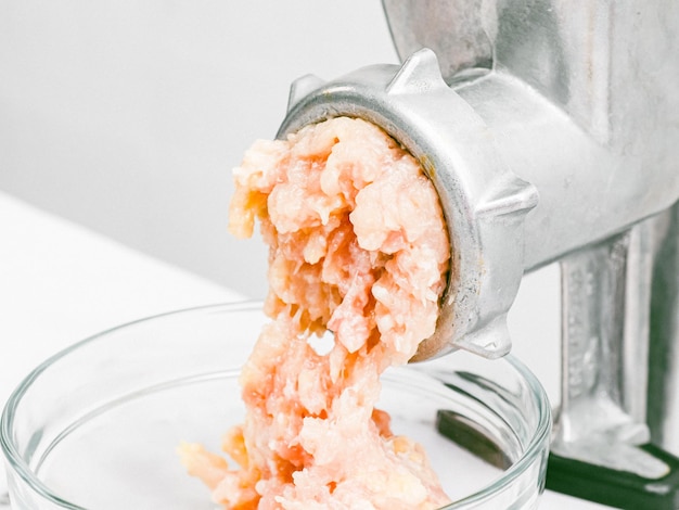 Manual meat grinder with minced meat in a glass dish on a marble table