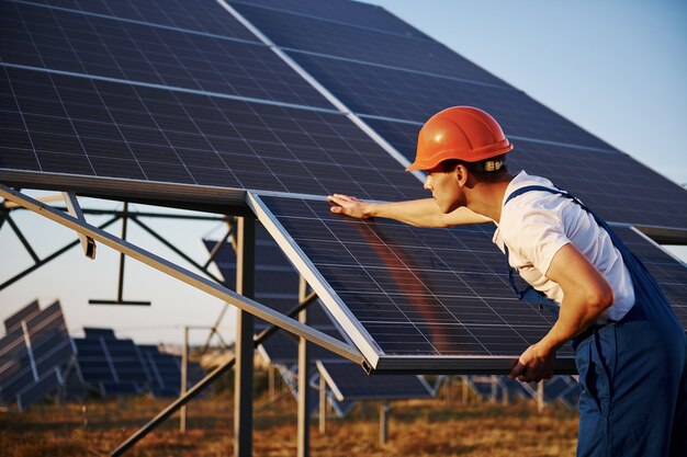 Manual work. Male worker in blue uniform outdoors with solar batteries at sunny day.