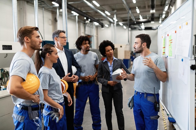 Photo manual worker communicating with company leaders and his coworkers during business presentation in a factory