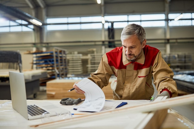 Manual worker going through paperwork while working at carpentry workshop