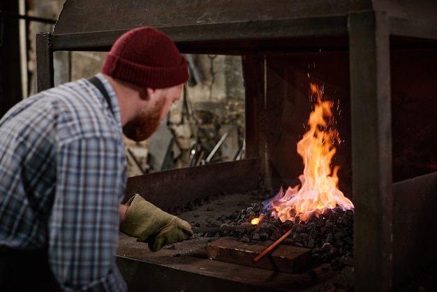 Manual worker in protective gloves adding coals to burn the flame in the furnace