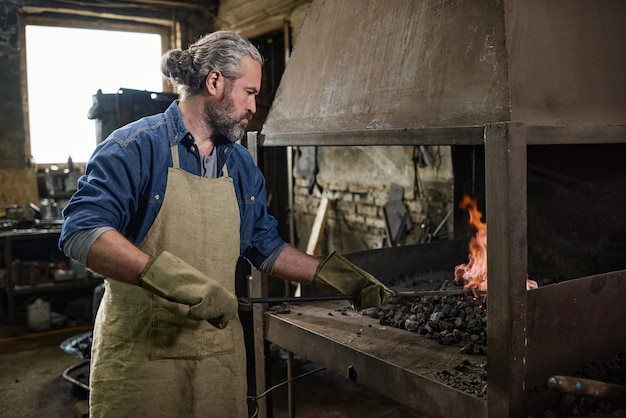 Manual worker putting the coal in the furnace and burning the fire in the workshop