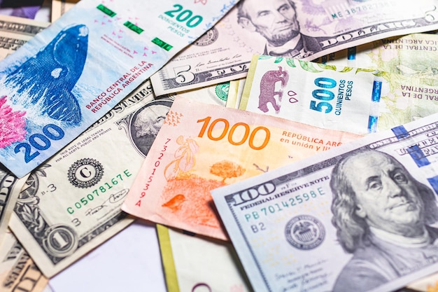 Molte banconote in pesos argentini con dollari usa sparsi per il concetto di cambio di denaro