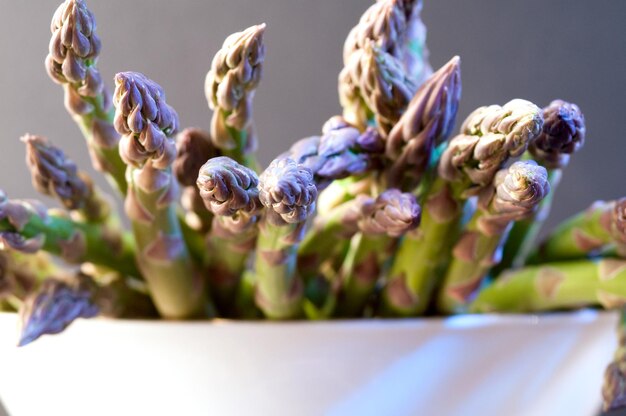 Foto molti asparagi su un piatto di legno su uno sfondo grigio tiro in studio di cibo vegetale sano