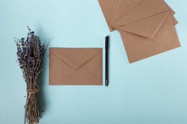 Many beige envelopes a black handle and dried lavender are beautifully laid out in a delicate blue b...