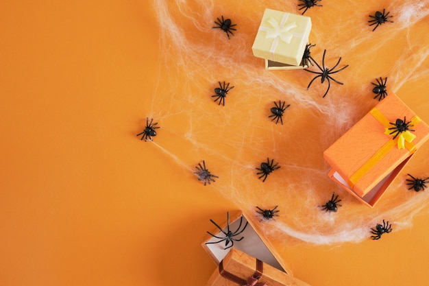 Many black plastic spiders and several gift boxes in a spider web on an orange background copy space