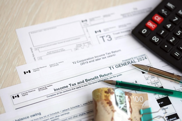 Many blank canadian tax forms lies on table with canadian money bills calculator and pen close up